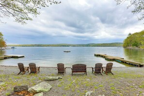 Uitzicht op een meer met houten stoelen gericht op het water, een steiger en een boot in de verte.