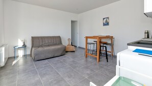 Una sala de estar moderna con un sofá gris, una mesita y una zona de cocina con un refrigerador blanco.