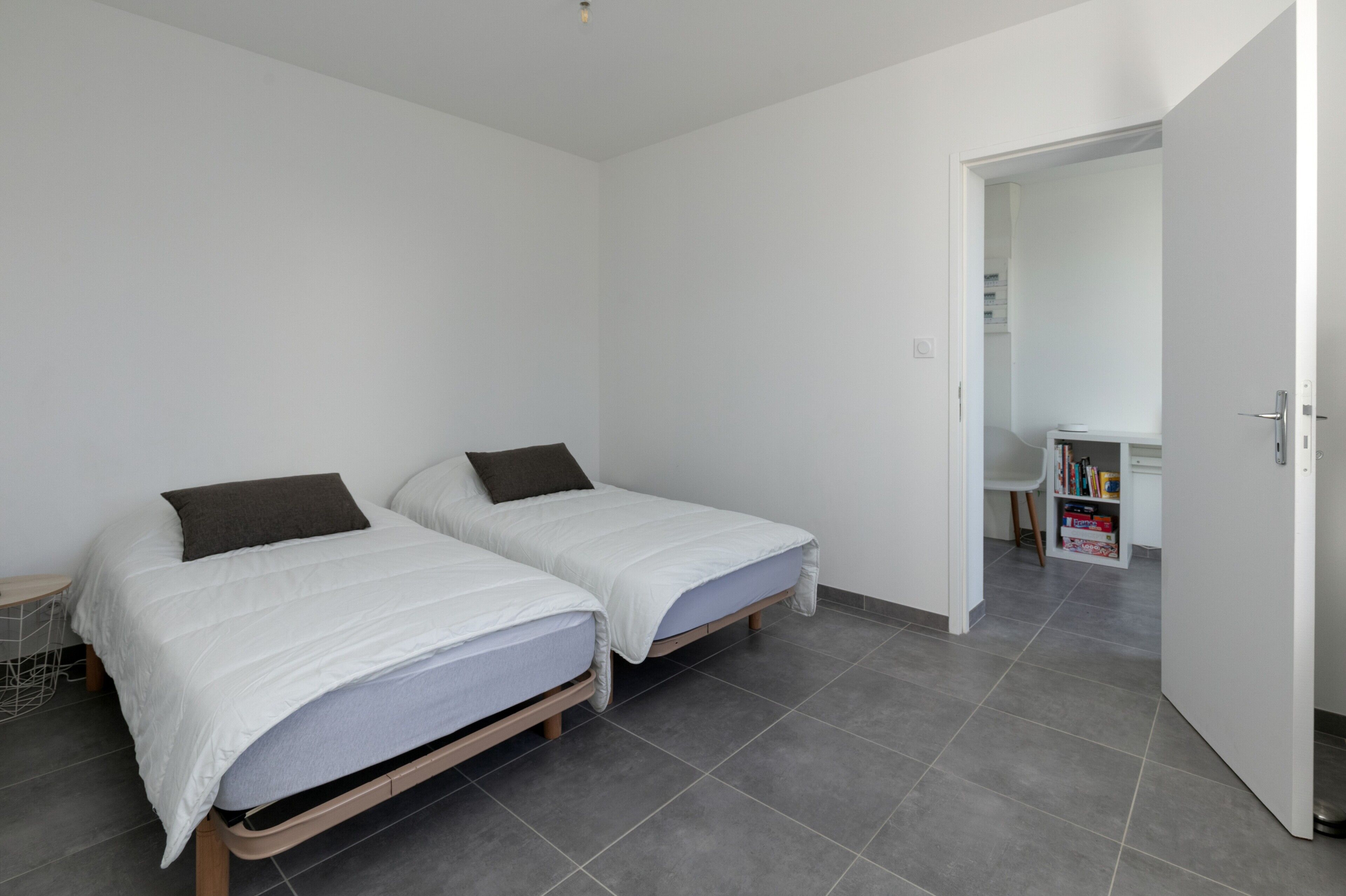 A bedroom with two beds, a white door, and a hallway leading to a bathroom.