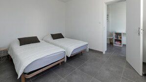 Un dormitorio con dos camas, una puerta blanca y un pasillo que da a un baño.