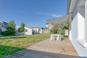 Une terrasse avec une table et des chaises, un bâtiment blanc et un ciel bleu dégagé.