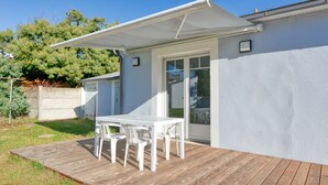 Un patio con mesa y sillas, una zona cubierta y un edificio con puerta y ventanas.