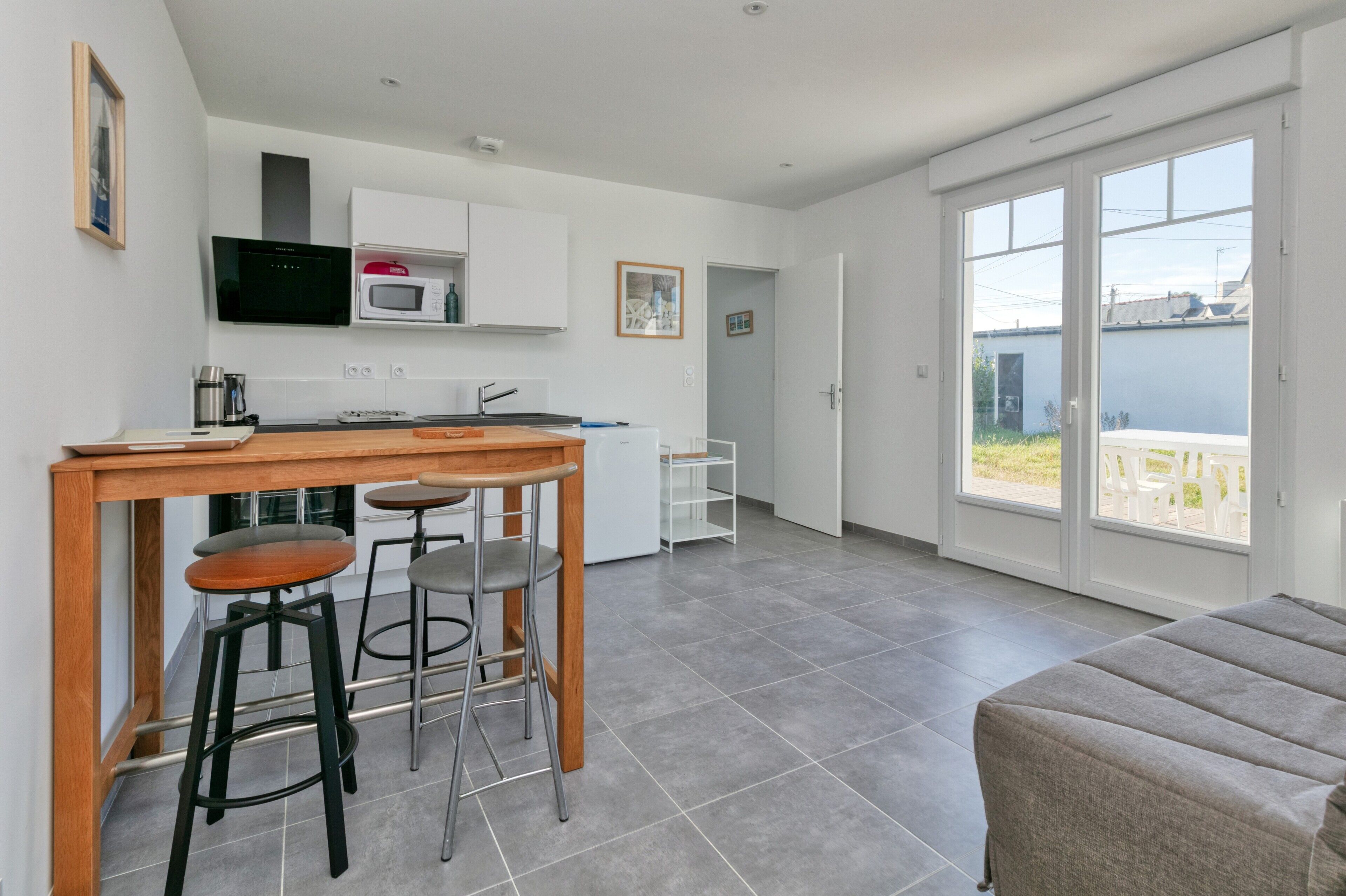 A modern kitchen with a dining area, a sofa, and a sliding glass door leading to an outdoor patio.