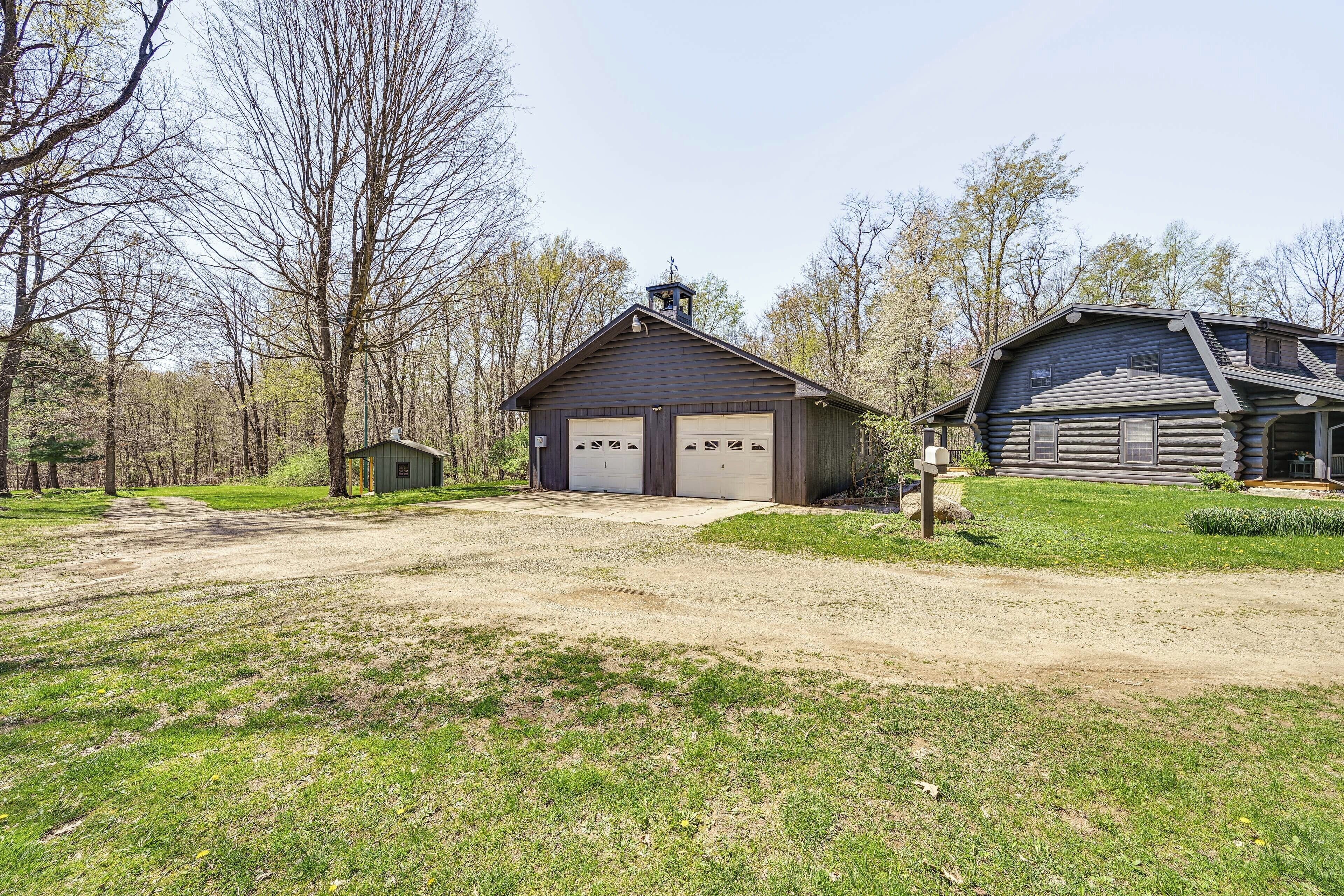 A rustic cabin with a garage, surrounded by trees and a grassy area.