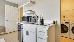 Ett kompakt kök med diskmaskin, mikrovågsugn och inbyggd ugn. Det finns en liten arbetsbänk med en diskho och en hylla ovanför.