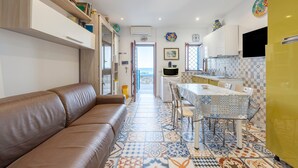 A modern kitchen with a dining area, a brown leather sofa, and a tiled floor.