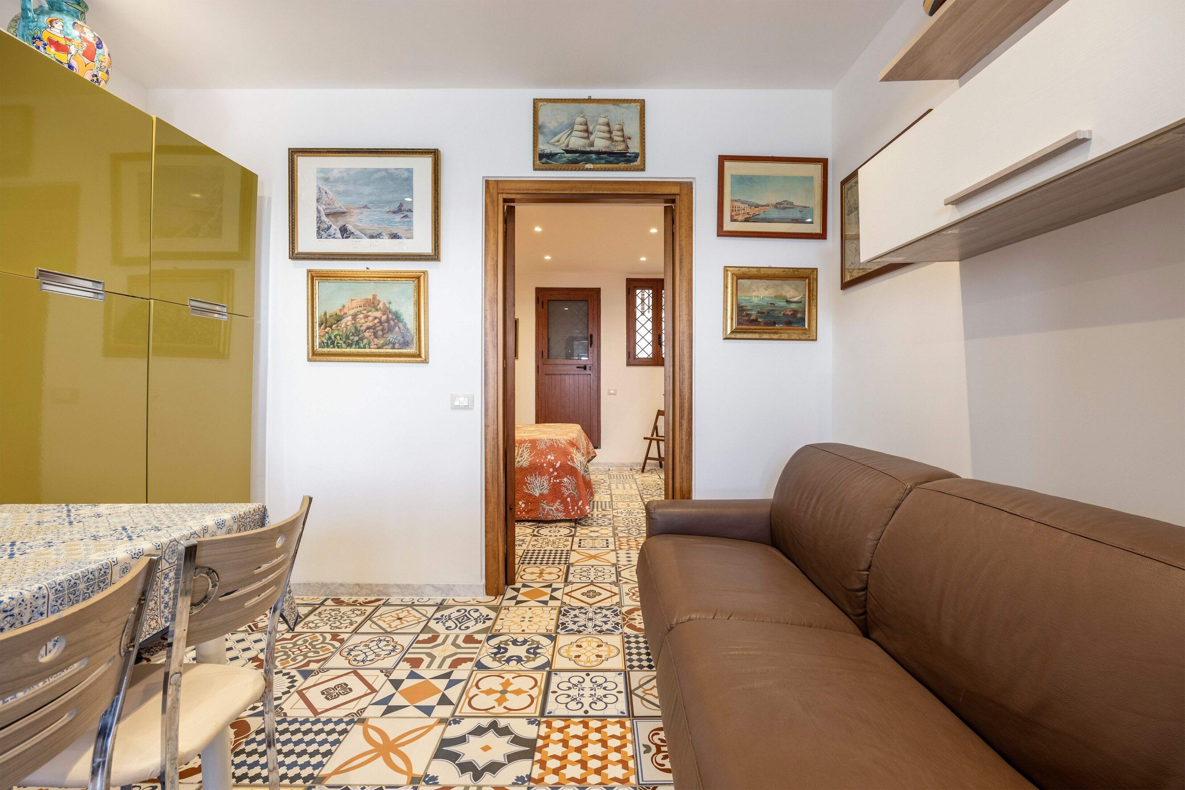 Ein Zimmer mit einem braunen Sofa, einem Esstisch mit Stühlen, einem gemusterten Boden und mehreren gerahmten Bildern an den Wänden.
