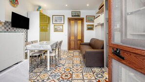 A compact living space with a dining area, a sofa, a TV mounted on the wall, and a patterned floor.
