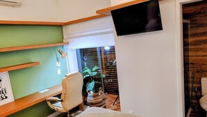 A compact room with a bed, a desk, a chair, a TV, and a window overlooking a balcony. - JYXDYJYJYGJYGJGYJ (Centro Florianópolis)