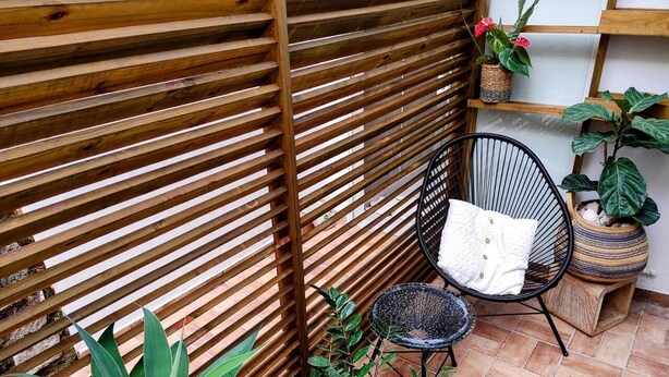 A patio area with a wooden slatted fence, a black woven chair, a small round table, and various potted plants. - JYXDYJYJYGJYGJGYJ (Centro Florianópolis)