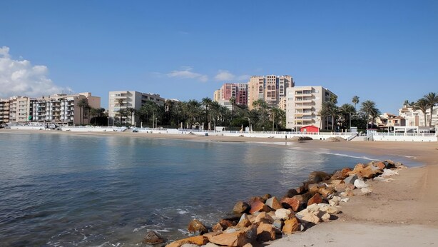 Un paisaje urbano costero con edificios, una playa y un litoral rocoso.