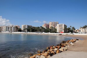 A coastal cityscape with buildings, a beach, and a rocky shoreline.