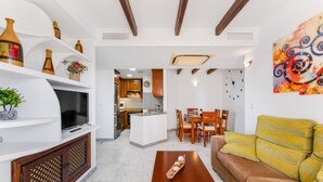 Una sala de estar con televisor, armarios de madera, un sofá y un comedor con sillas y una mesa.