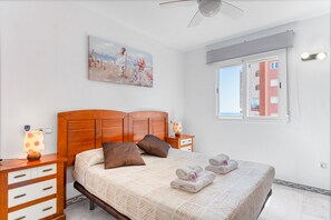 Un dormitorio con cabecera de madera, un cuadro de una mujer con bicicleta, una ventana con vista a edificios y una cama con toallas.