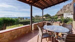 Un espace extérieur abrité, doté d’une table et de chaises, de murs en pierre et offrant une vue sur la mer et les montagnes.