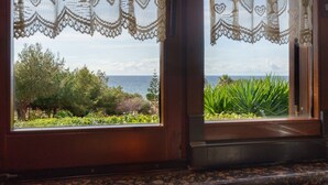 Une fenêtre ornée de rideaux en dentelle, d’où l’on peut admirer la mer et la verdure.