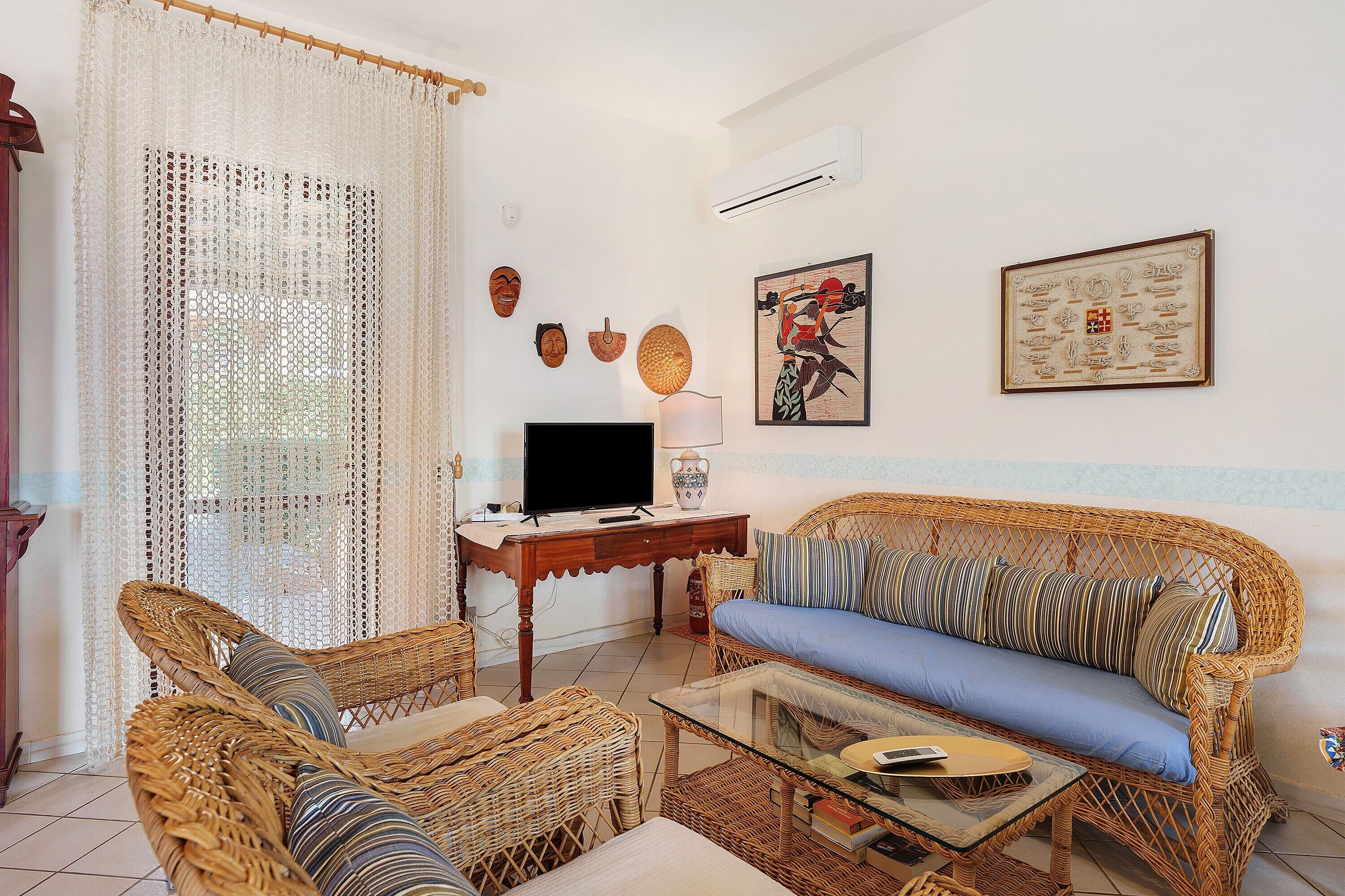 A living room with wicker furniture, a glass coffee table, a television, and decorative items on the wall.