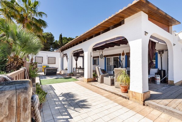 A covered outdoor patio with seating, a wooden pergola, and a white building with arches.