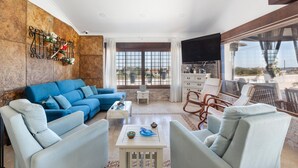 Un salon avec un canapé bleu, des fauteuils blancs, une table basse et un téléviseur.