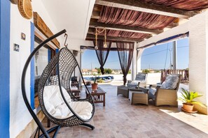 A patio with wicker furniture, a hanging chair, and a view of the sea.