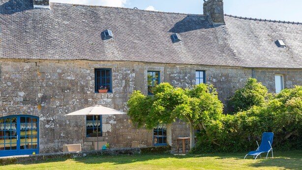 Un bâtiment en pierre avec un toit en tuiles, une chaise bleue et une petite table dans la cour.