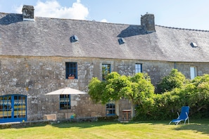 Un bâtiment en pierre avec un toit en tuiles, une chaise bleue et une petite table dans la cour.