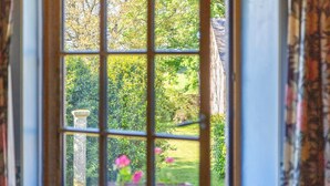 Une fenêtre donnant sur un jardin, un pilier en pierre et une plante en pot.