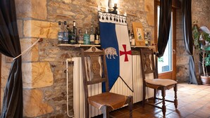Une pièce aux murs de pierre, avec une chaise en bois, un drapeau et une étagère remplie de bouteilles.