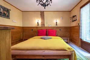Un lit en bois avec un couvre-lit jaune et des oreillers rouges, deux lampes fixées au mur et une tête de lit en bois.