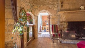 Un pasillo de paredes de piedra que conduce a una habitación con chimenea, suelo de baldosas y una planta.