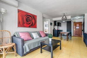 A living room with a sofa, a coffee table, a dining table, and a kitchen area in the background. - Apartment 'Rincon Del Arenal' with Sea View, Wi-Fi and Air Conditioning (Platja de l'Arenal)