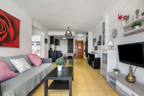 A modern living room with a sofa, coffee table, TV, and kitchen in the background. - Apartment 'Rincon Del Arenal' with Sea View, Wi-Fi and Air Conditioning (Platja de l'Arenal)