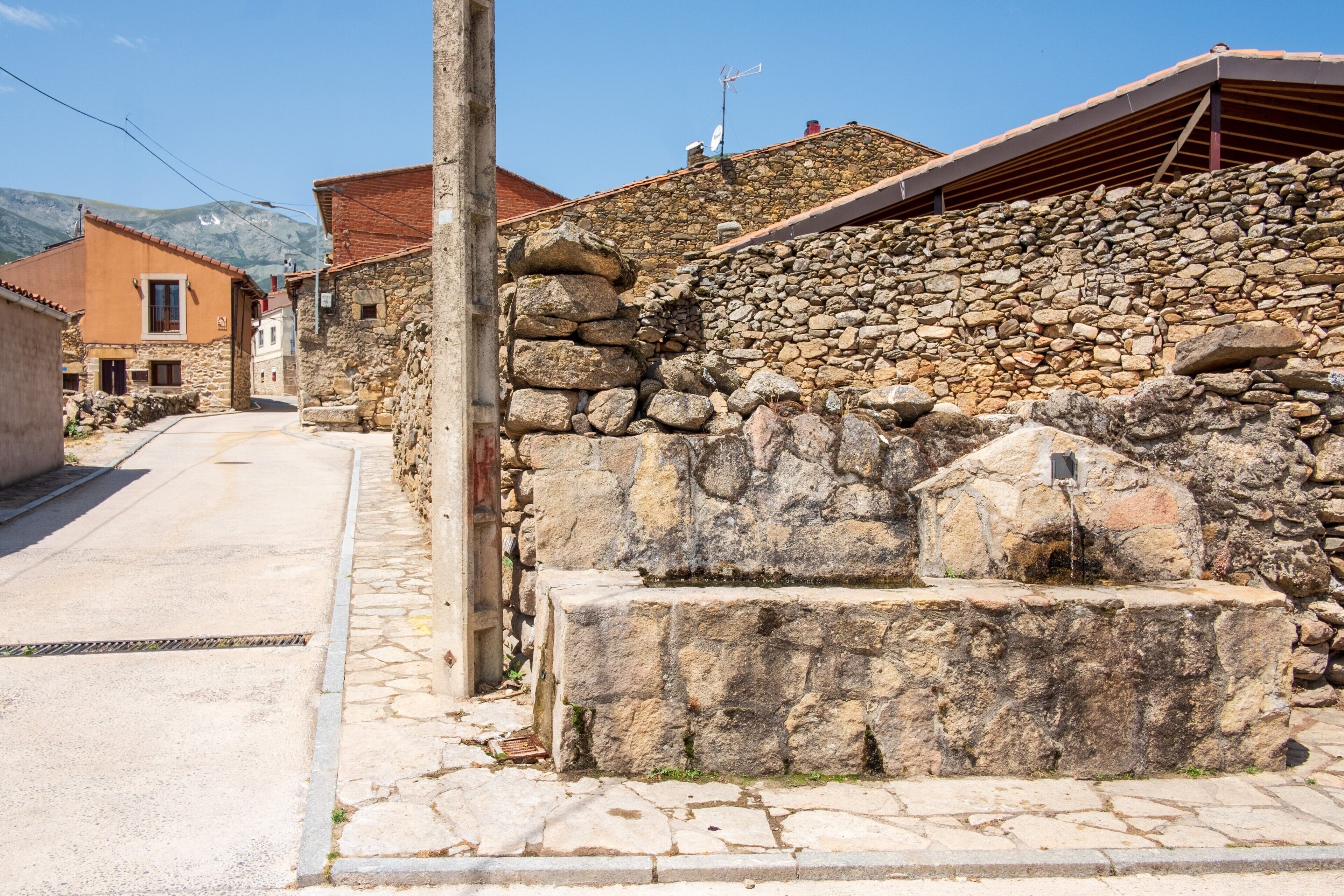 A stone wall with a water feature, a clear sky, and a mountain in the background.