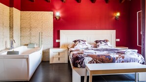 Une chambre à coucher avec un lit, des tables de chevet, une baignoire et un mur en pierre.