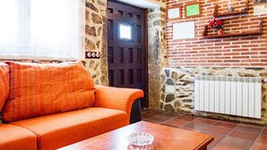 Une pièce avec un mur en pierre, une porte en bois, un mur en briques avec des étagères, un radiateur et un canapé avec des coussins orange.
