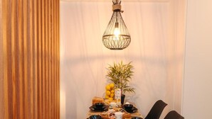 A dining area with a wooden ceiling, a hanging light fixture, a table set with plates, bowls, and a plant.