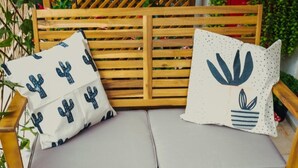 A wooden bench with cushions, a woven basket with snacks, and bottles on a table.