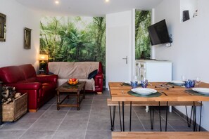 A living room with a red sofa, a wooden coffee table with fruit, and a dining area with a wooden table set for two.