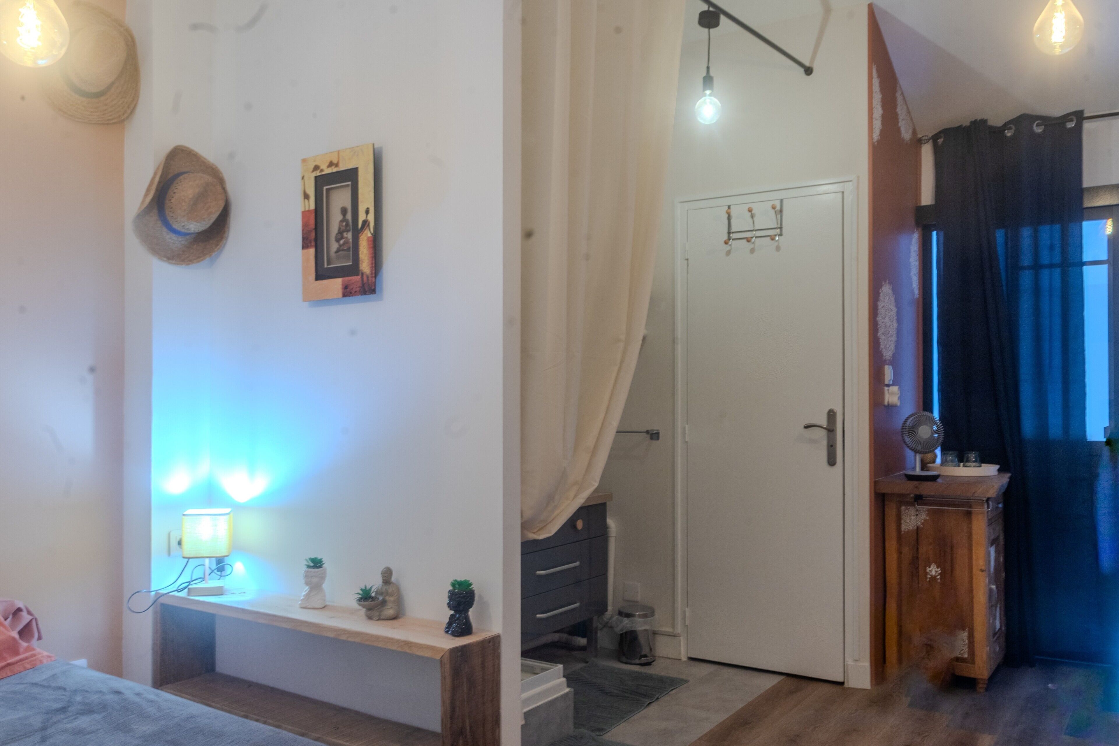 Een slaapkamer met een bed, nachtkastje, lamp, wanddecoratie en een deur naar een andere kamer.