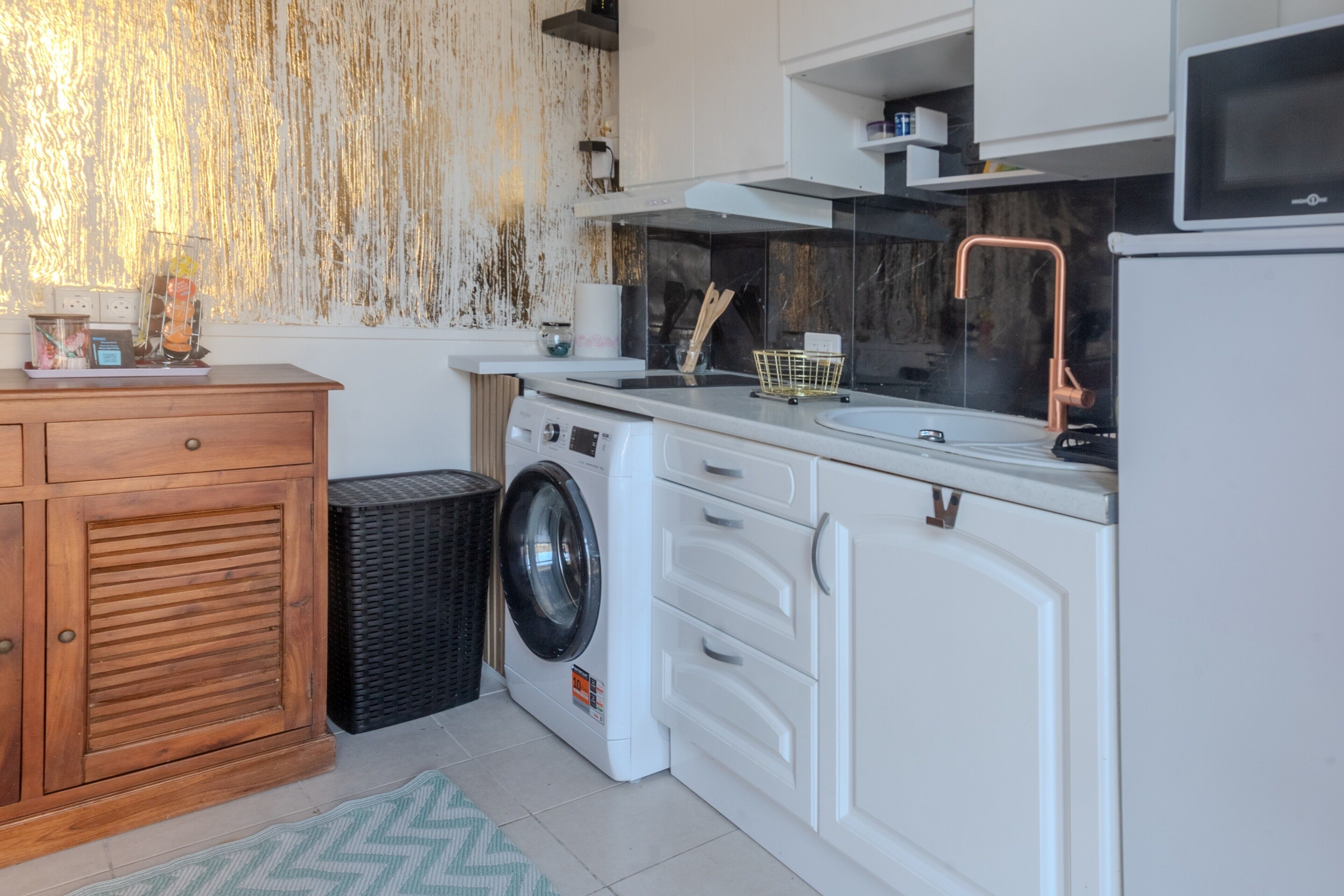 A compact kitchen with a washing machine, a microwave, and a sink with a copper faucet.