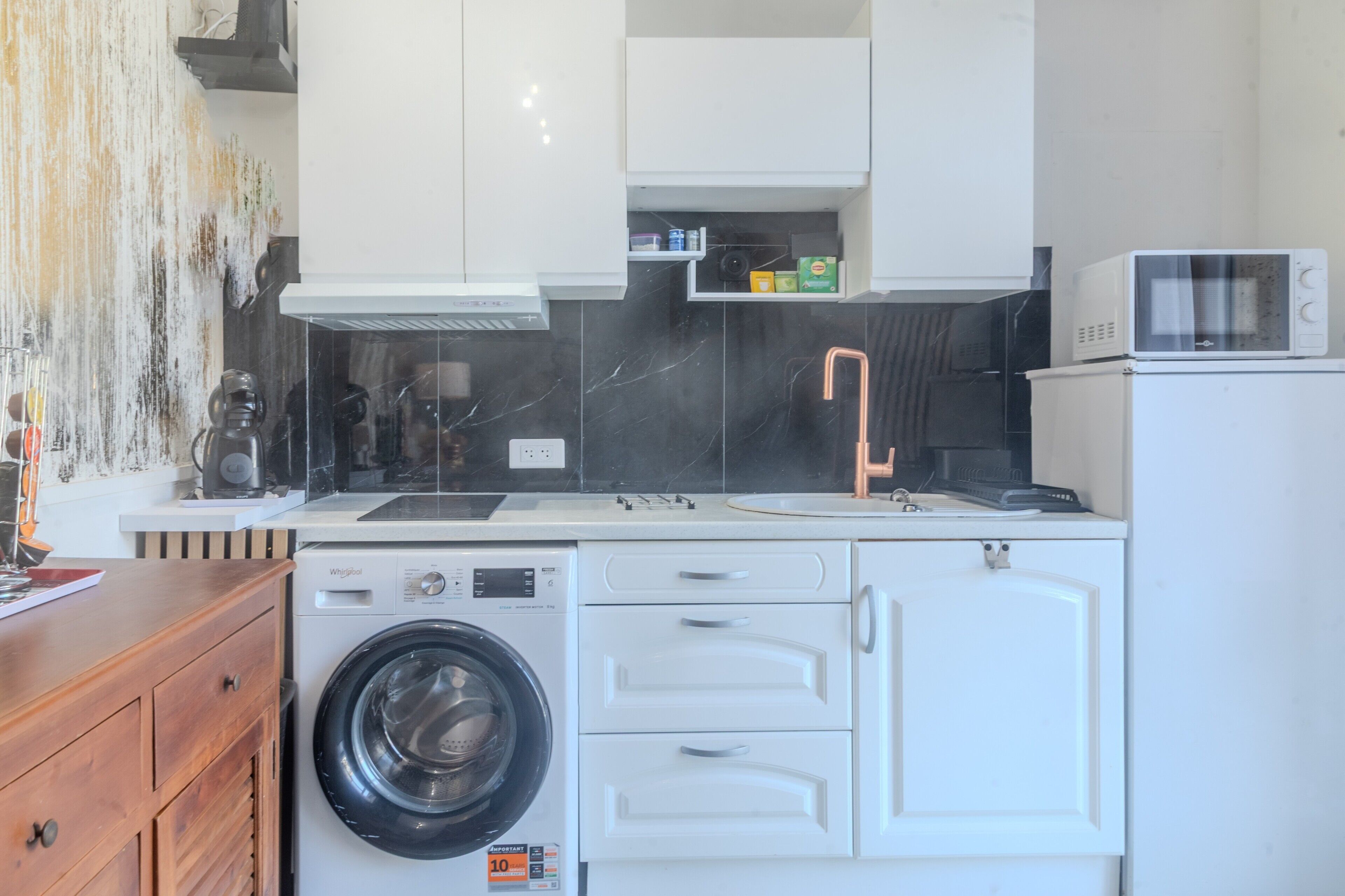 Une cuisine compacte équipée d’un lave-linge, d’un four à micro-ondes et de meubles de rangement blancs.