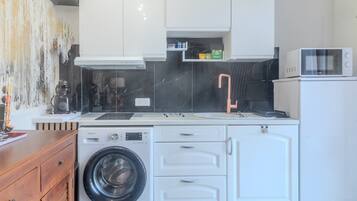 Une cuisine compacte équipée d’un lave-linge, d’un four à micro-ondes et de meubles de rangement blancs.
