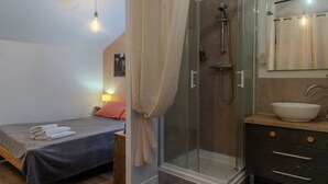 Ein Schlafzimmer mit Bett, Nachttisch, Dusche mit Glastür, Waschbecken und Spiegel.