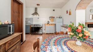 A kitchen with a stove, oven, and refrigerator, a dining table with a colorful tablecloth, and a vase with flowers.