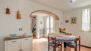 A dining area with a round table, chairs, and a decorative centerpiece. There is a staircase leading to an upper floor, and a white cabinet with drawers.