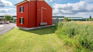 A small red building with a door and windows, surrounded by grass and a fence.