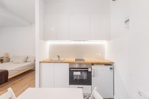 A compact kitchenette with a built-in oven, a sink, and a compact refrigerator. - Apartment 'Portblanc' with Balcony, Wi-Fi, and Air Conditioning (Arenys de Mar)