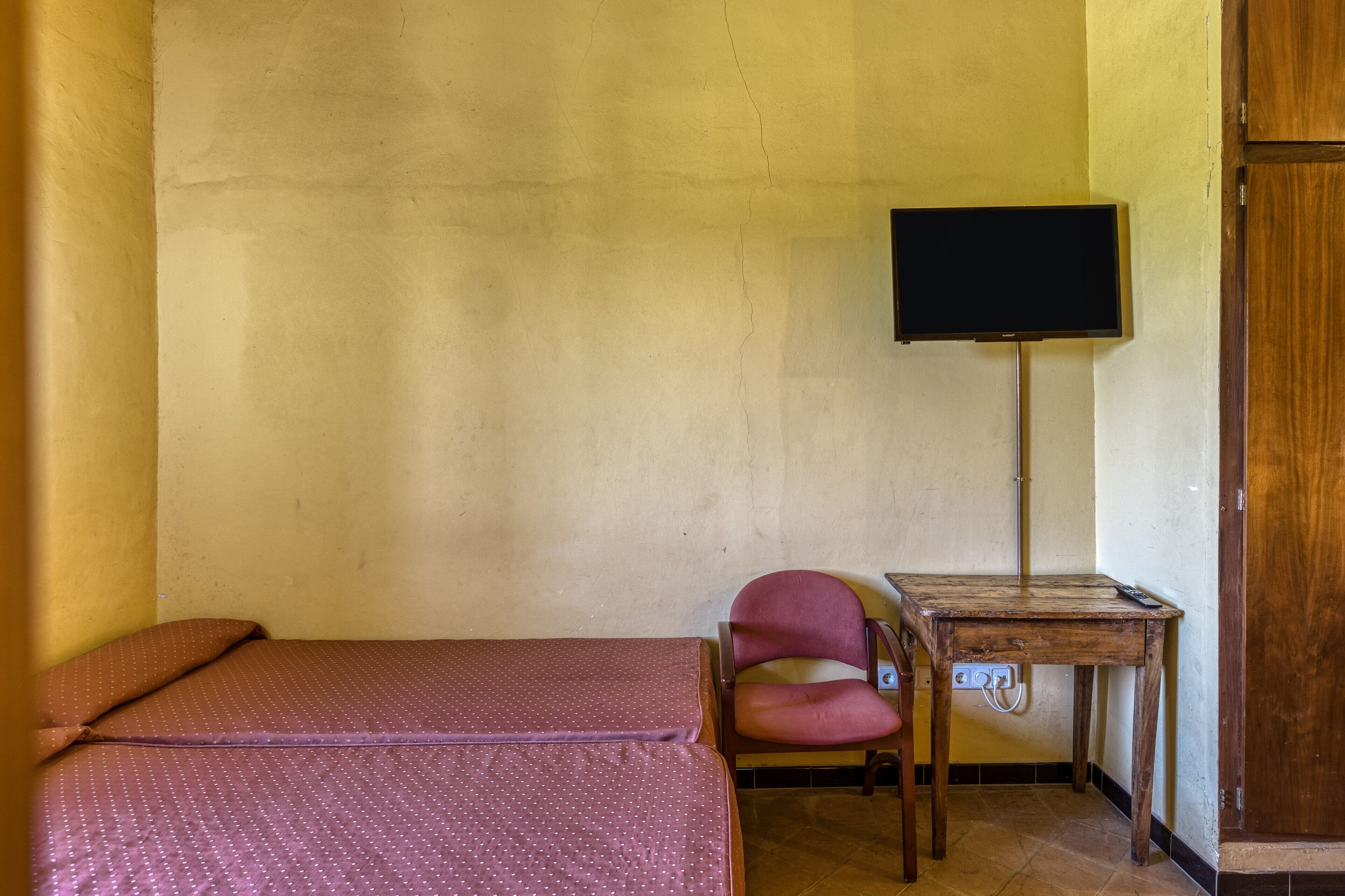 Una habitación con cama, una silla, una mesita y televisión.