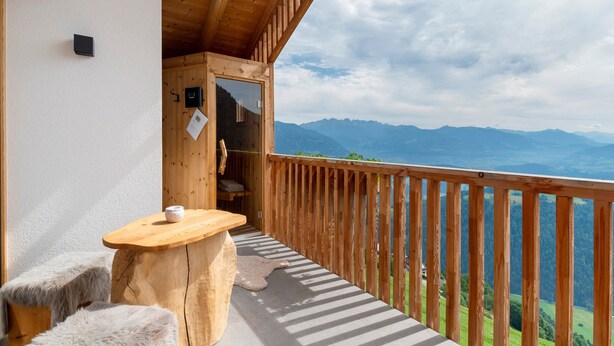 A wooden balcony with a view of mountains, a wooden table, and a small stool. - Apartment 'Prielerhof Sunrise' with Mountain View, Private Terrace and Wi-Fi (St. Lorenzen)