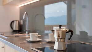 A kitchen with a coffee maker, cups, and a view of mountains through a window. - Apartment 'Prielerhof Sunrise' with Mountain View, Private Terrace and Wi-Fi (St. Lorenzen)